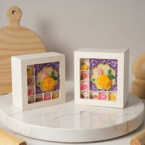 A square white gift boxes with floral window displays containing colorful miniature flowers, styled on a round white marble tray with wooden props in the background.